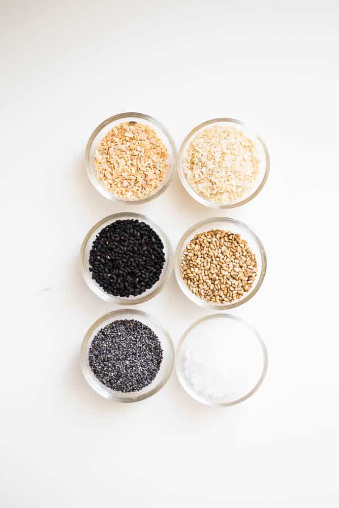 Very small glass prep bowls containing all six ingredients for everything bagel seasoning -- white sesame seeds, black sesame seeds, poppy seeds, sea salt flakes, dried minced onion, dried minced garlic.