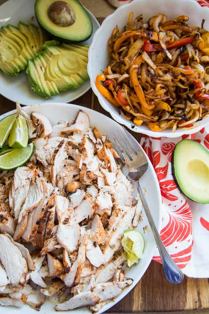 Bowls filled with finished sliced chicken fajita meat and grilled fajita vegetables ready to serve with sliced avocado.
