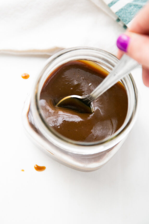 Thick, rich paleo salted caramel sauce in a glass jar with a spoon ready to scoop.