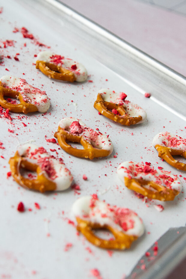 Strawberry White Chocolate Pretzels drying on a parchment-lined baking sheet.