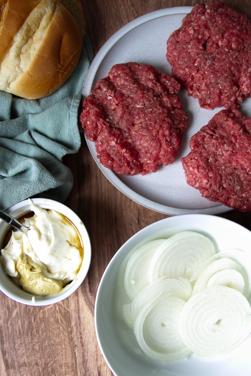 Patties formed, onions sliced, and aioli ingredients in a small bowl. 