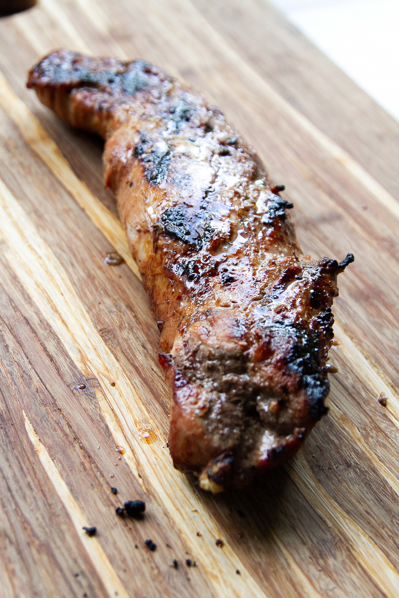 Grilled and glazed pork tenderloin resting on a cutting board.