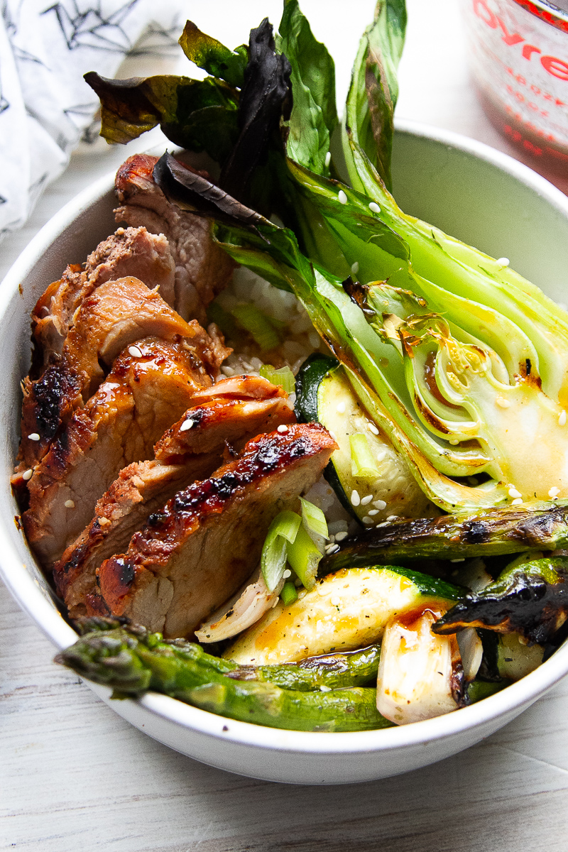 Bowl with sliced pork tenderloin, rice, and grilled vegetables.