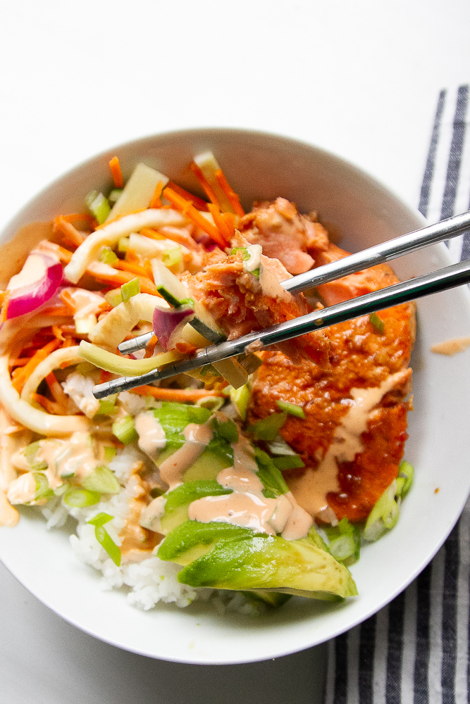 A finished salmon rice bowl with a pair of stainless steel chopsticks grabbing a bit out of the center.