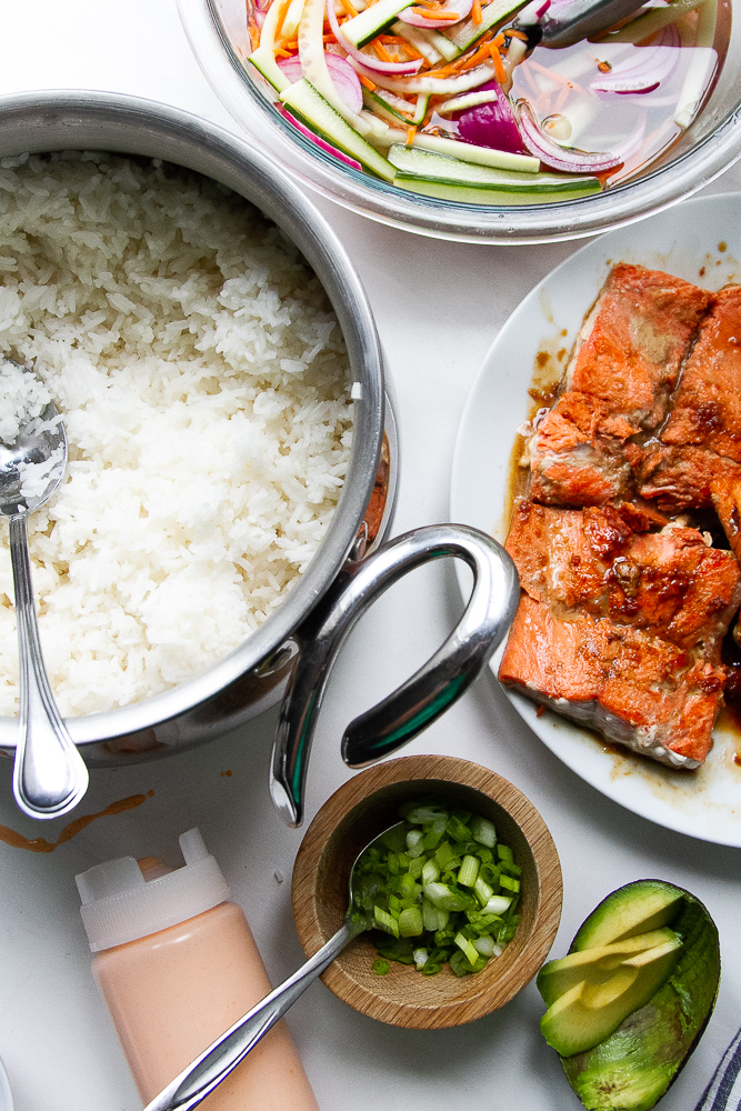 Components ready to assemble the bowls -- steamed rice, glazed salmon, pickled vegetables, spicy mayo, green onions, and avocado.