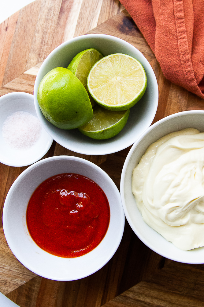 Ingredients for the spicy mayo in little white bowls: mayo, sriracha, salt, and halved limes.