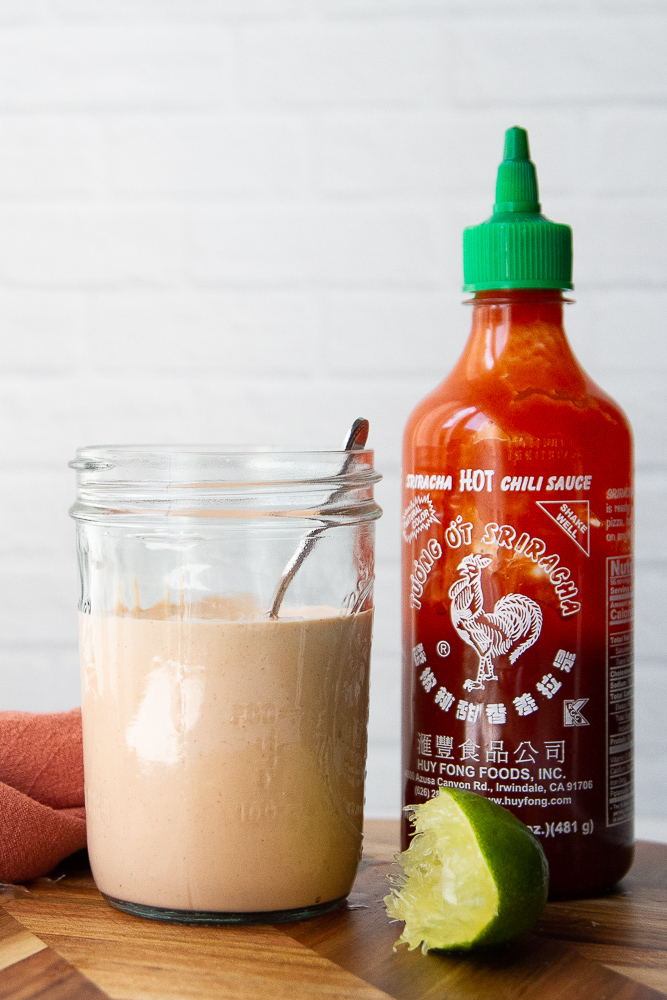 Sauce in a mason jar sitting next to a bottle of rooster sauce.