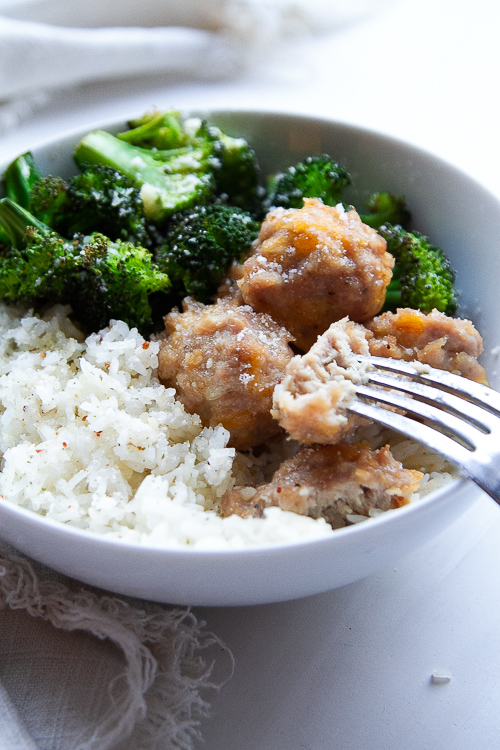 Baked chicken meatballs in a bowl with seasoned rice and roasted broccoli.