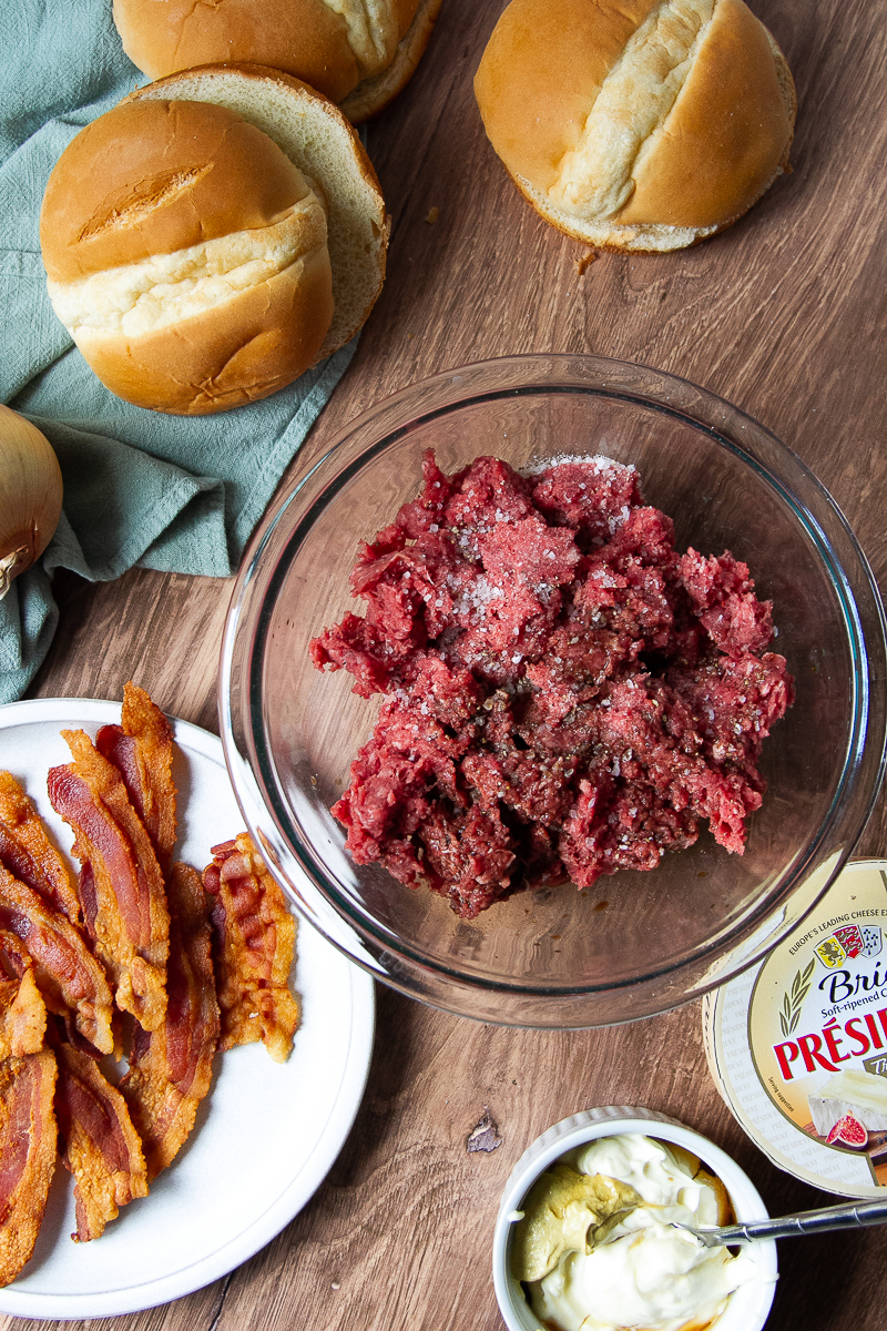Ingredients for the bison burgers: ground meat, bacon, brie, aioli, buns, and onions.