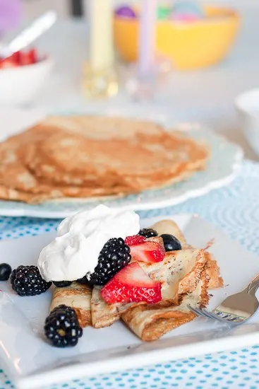 Crepes topped with strawberries, blackberries, and whipped cream on a white plate.