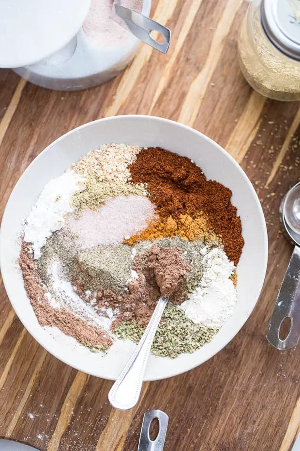 The Best Homemade Taco Seasoning! Photo shows a myriad of spices loosely blended in a white bowl with a silver spoon.