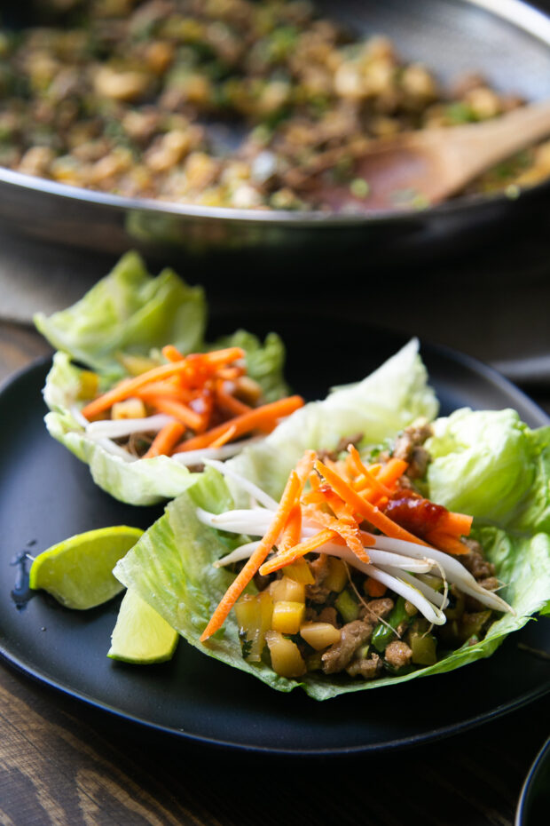 Two Thai Chicken Lettuce Wraps on a black plate with lime wedges on the side.