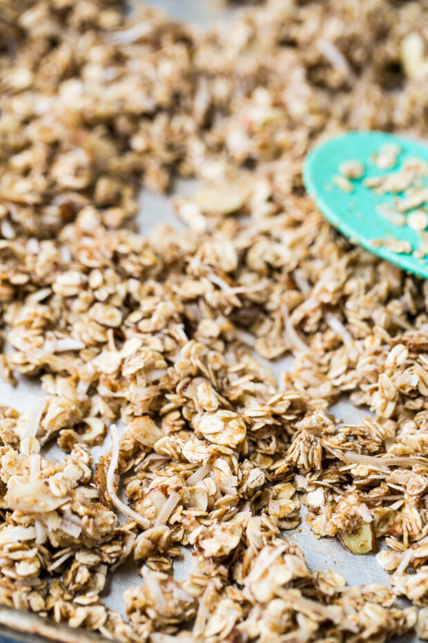 Wet granola mixture being spread out on a large baking sheet.