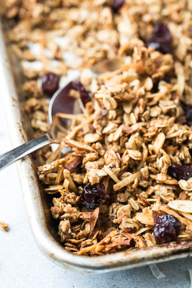 Finished, baked granola on a rimmed baking sheet with dried cranberries added.