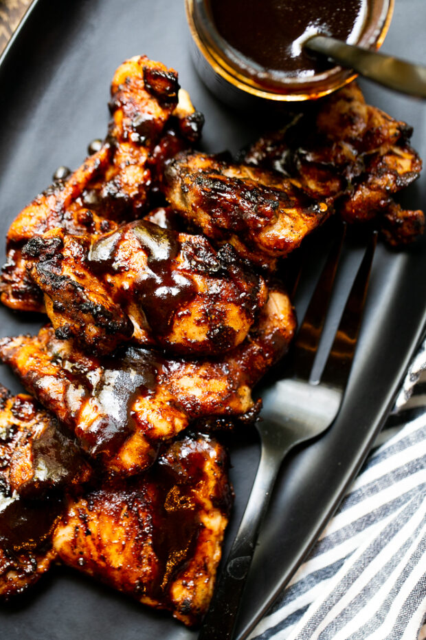 Easy Grilled BBQ Chicken on a black platter drizzled with BBQ sauce.