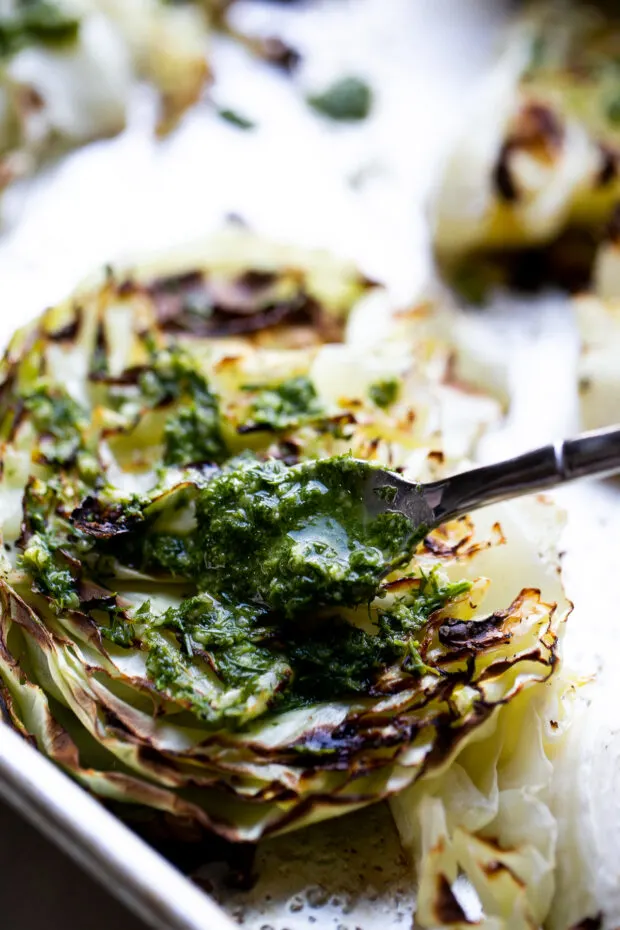 A small spoonful of pesto is being smeared on a roasted cabbage steak.