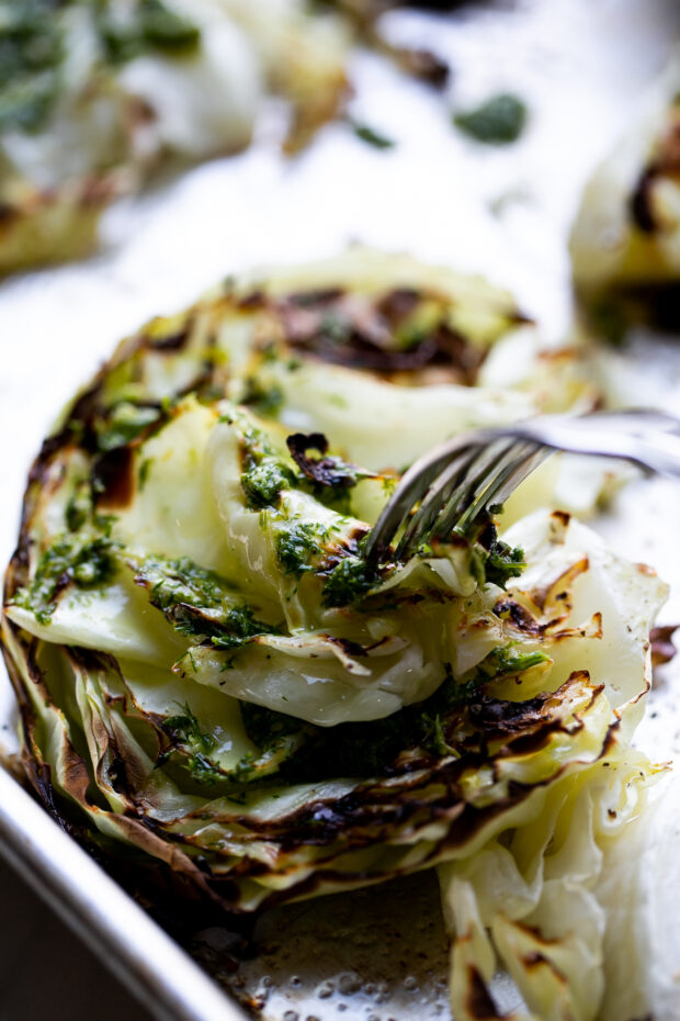 Roasted cabbage steak topped with dill pesto. A fork is taking a bit out of the center and the leaves are folded.