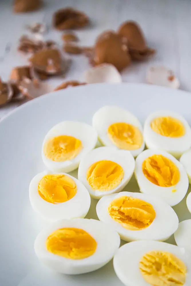 Hard-cooked eggs ready to go into Egg Curry A plate of hard-cooked eggs that have been peeled and sliced in half.