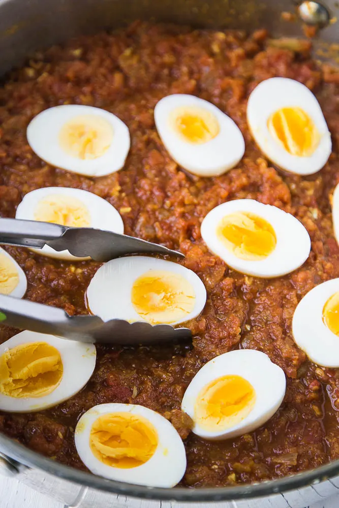 Add the eggs to the curry sauce and let them cook and absorb some of those delicious Indian spices. Hard cooked eggs that have been added to the skillet of curry sauce, cut-side up.