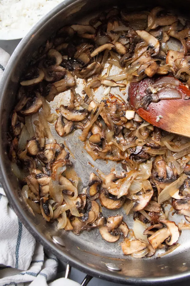 Large stainless skillet with caramelized mushrooms and onions.