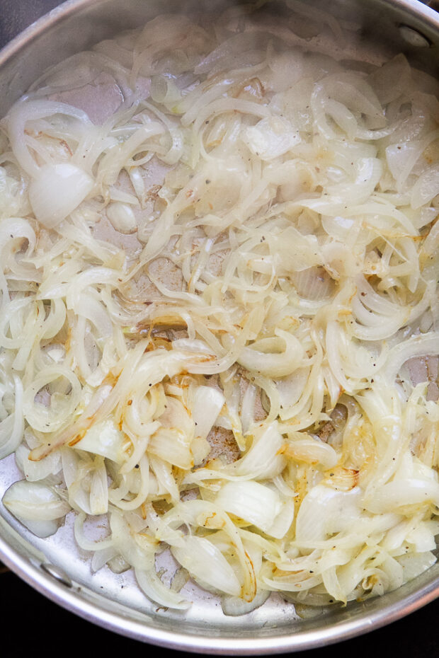 Shot of some onions being sautéed in a stainless steel skillet. They're just starting to turn a little golden brown.