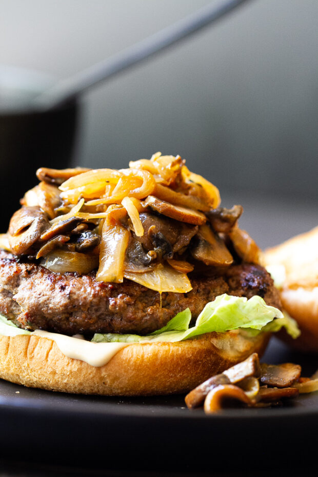 Chipotle Caramelized Onion & Mushroom Burger on a plate. Burger does not have the top bun so you can see the onions and mushrooms piled up on the burger patty.