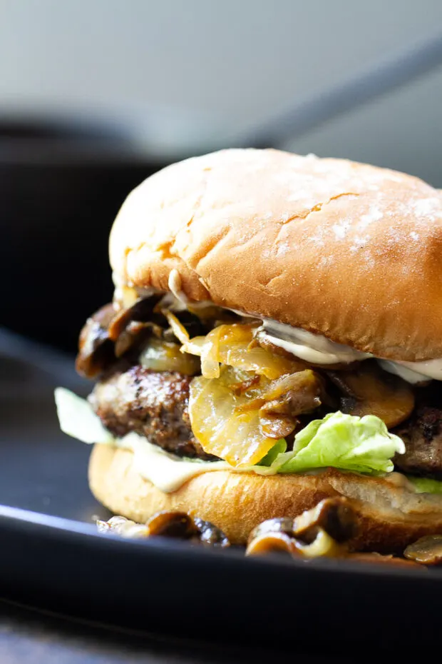 Complete burger with the top bun. Mushrooms and onions are falling out of the sides.