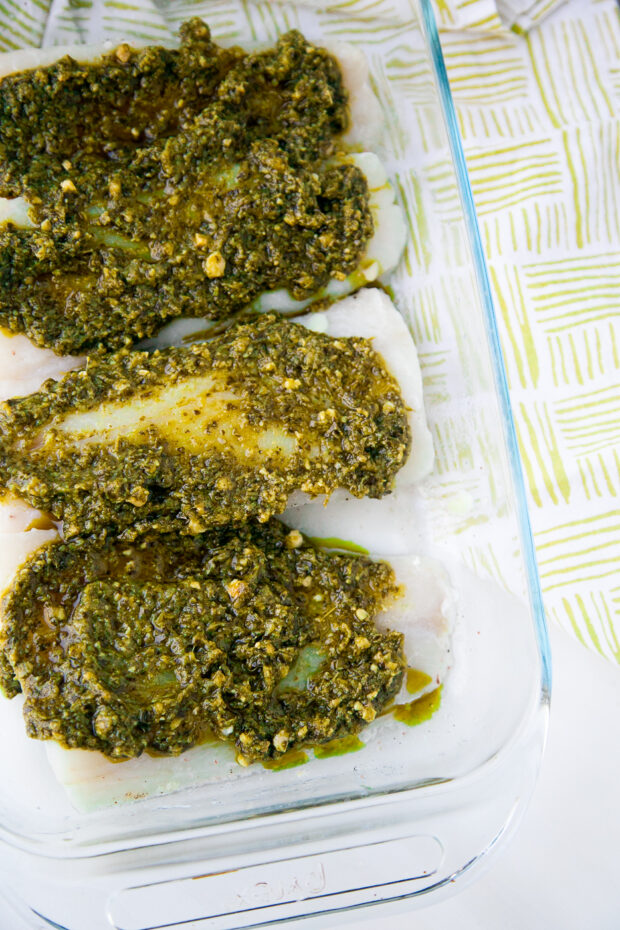 Raw cod fillets in a glass dish covered with pesto.