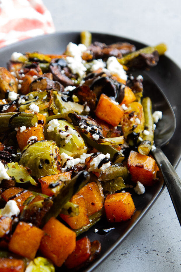 Balsamic Roasted Vegetables sprinkled with feta and drizzled with balsamic glaze on a black serving platter.