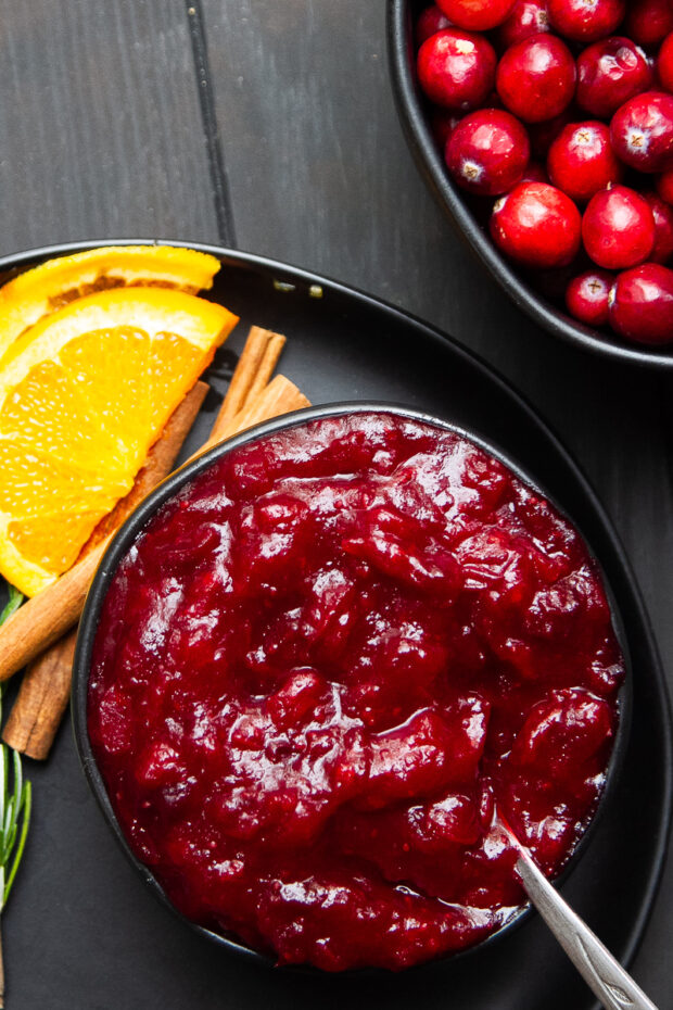 Finished healthy cranberry sauce in a serving bowl next to a bowl fresh cranberries.
