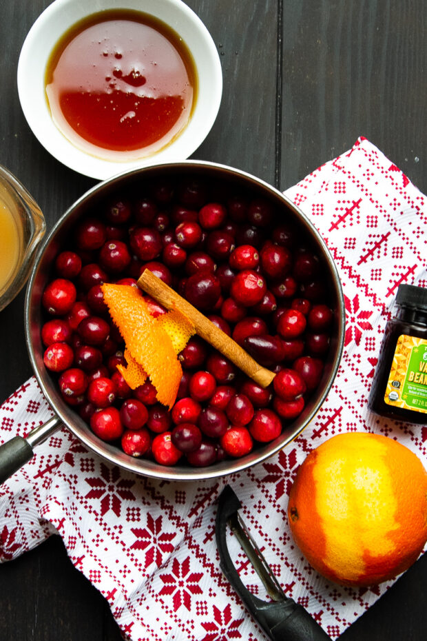 homemade cranberry sauce ingredients -- fresh, whole cranberries, orange, cinnamon stick, cider, maple syrup, vanilla bean paste.