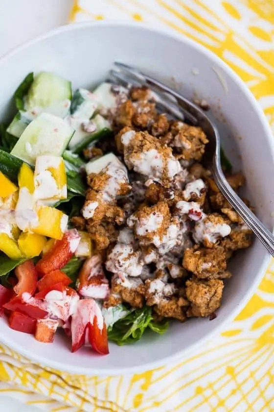 A bowl with Chipotle Copycat Chorizo over greens with vegetables and dressing on top.