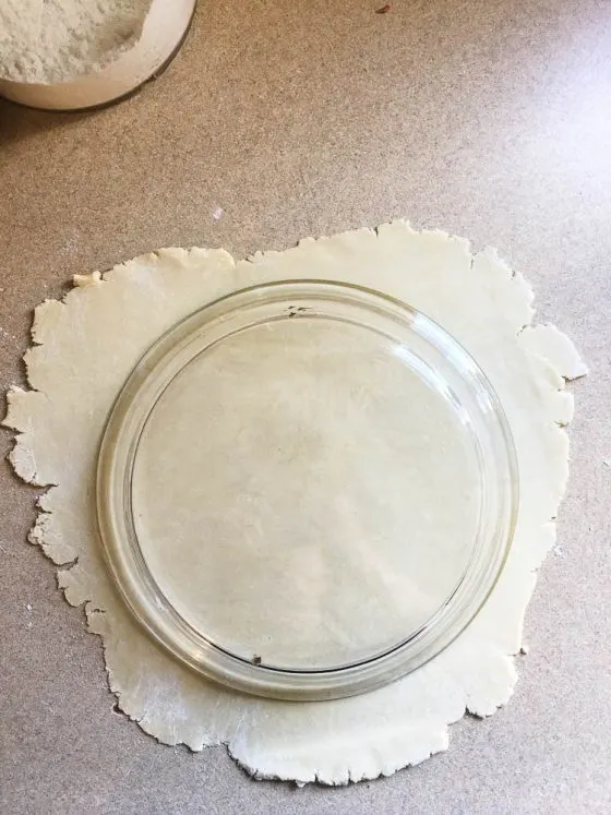 Pie crust dough rolled out on a counter with an upside down pie crust dish on top to measure.