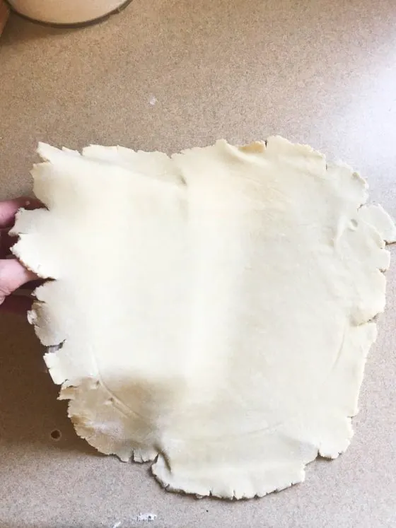 Pie crust dough being lifted by the pastry cutter.