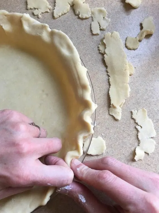 View of the pie crust dough being trimmed and crimped. 