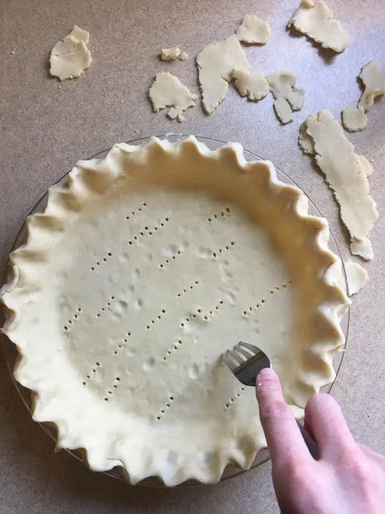 Trimmed and crimped pie crust dough with fork pricks in the bottom to keep it from bubbling while it's pre-baked.