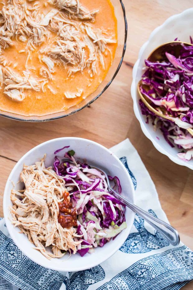 Bowl of shredded red curry chicken with purple cabbage slaw and some sambal oelek chili paste.