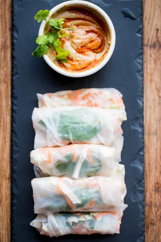 Thai chicken spring rolls on a black stone platter with a ramekin of spicy peanut sauce.