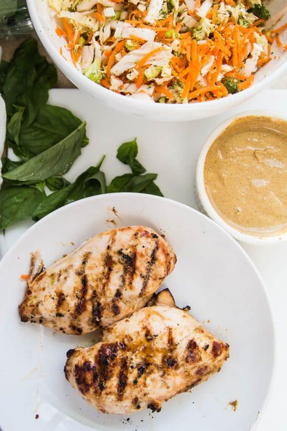 A plate with Thai marinated grilled chicken next to a ramekin of peanut sauce and a bowl full of the vegetable mixture.