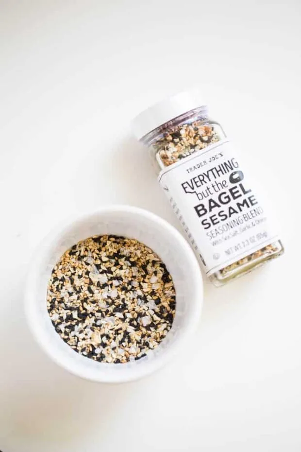 A ramekin with everything bagel seasoning next to a glass jar of Trader Joe's Everything but the Bagel Seasoning
