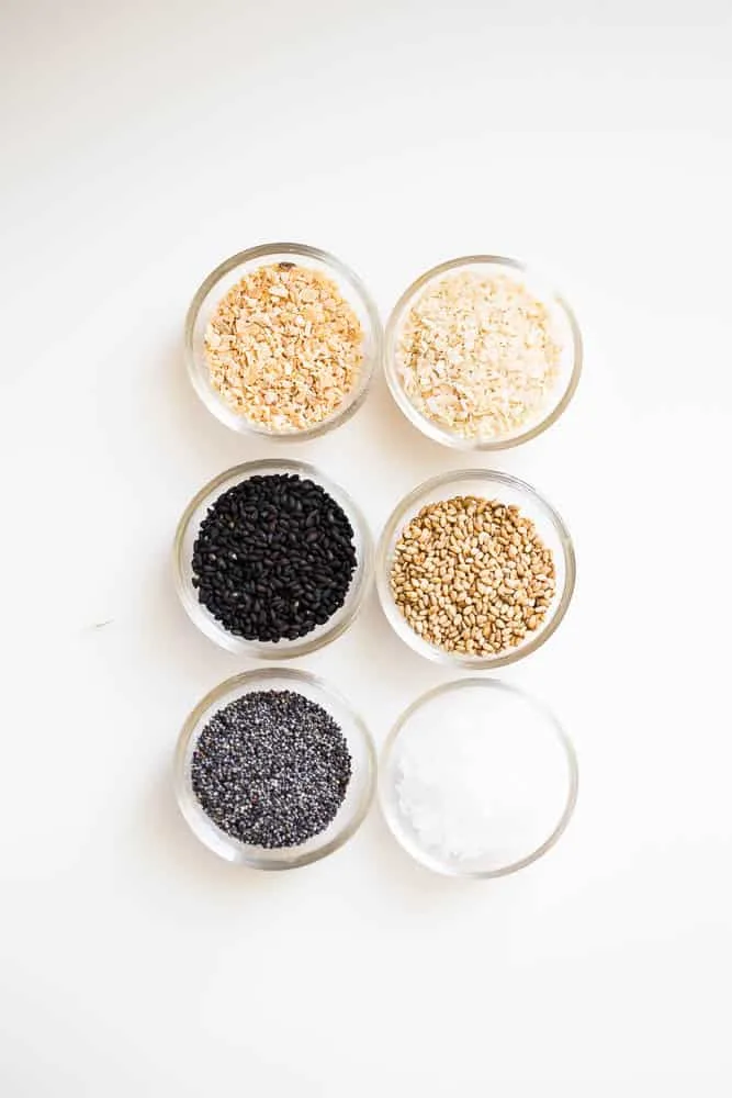 Very small glass prep bowls containing all six ingredients for everything bagel seasoning -- white sesame seeds, black sesame seeds, poppy seeds, sea salt flakes, dried minced onion, dried minced garlic.