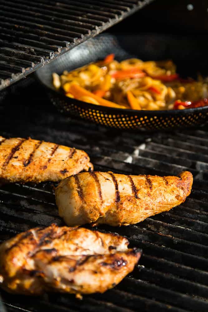 A view from the grill -- chicken breasts with dark grill marks and a grill pan filled with pepper and onions.