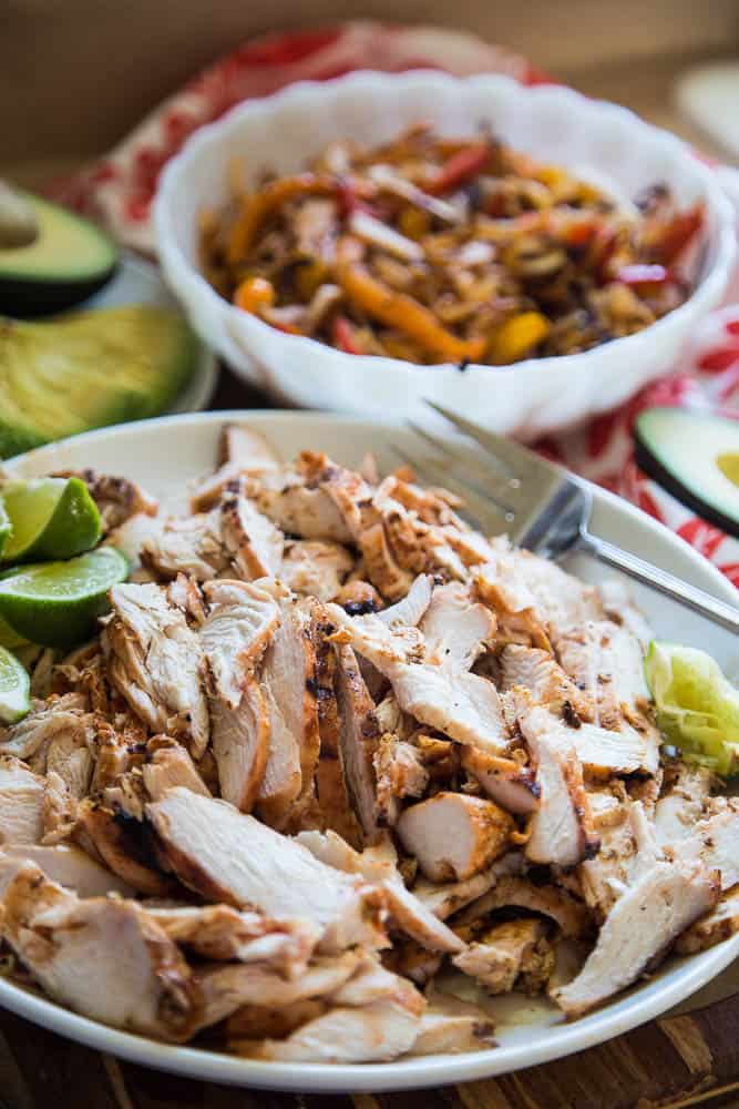 Sliced chicken fajita meat with a bowl of fajita veggies with fresh lime wedges ready to serve!