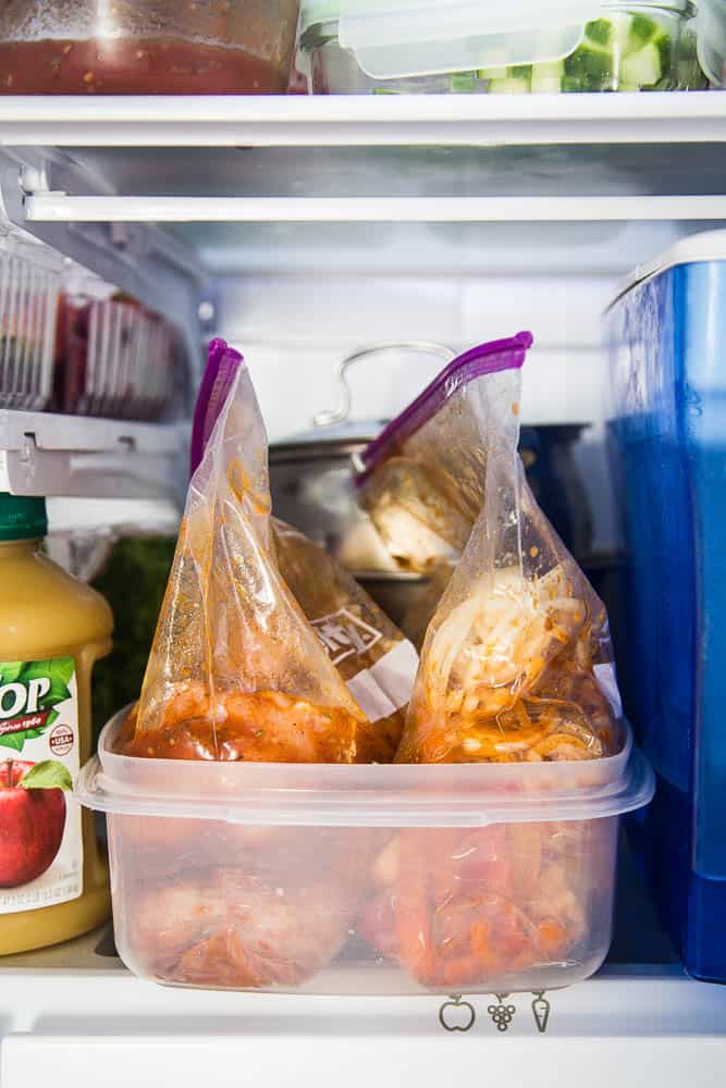 Two plastic ziptop bags, one with chicken breasts, and the other with sliced onions and bell peppers. Everything is tossed in fajita marinade.