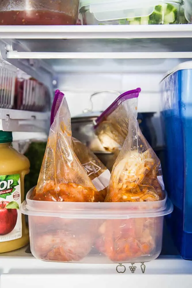 Two plastic ziptop bags, one with chicken breasts, and the other with sliced onions and bell peppers. Everything is tossed in fajita marinade.