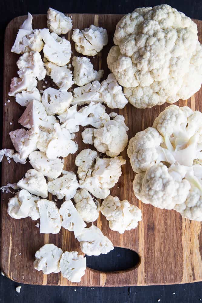 Cutting board with three heads of cauliflower -- one is cut into florets.