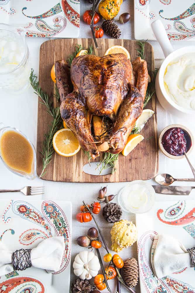 Beautiful Dry Brine Turkey with Herb Butter on a wooden cutting board garnished with rosemary and oranges.