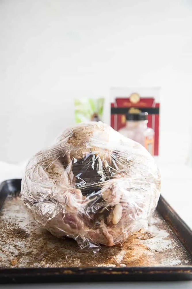 Uncooked turkey that has been rubbed with dry brine seasonings and wrapped in plastic wrap -- ready for the fridge.