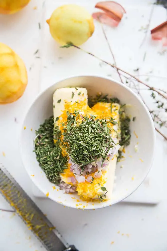 Two sticks of butter in a bowl with orange zest, shallots, garlic, and fresh rosemary.