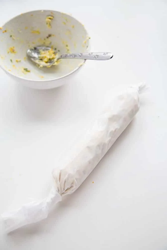 Herb butter that has been rolled into a tube in the parchment with the ends twisted together. Ready to be chilled.